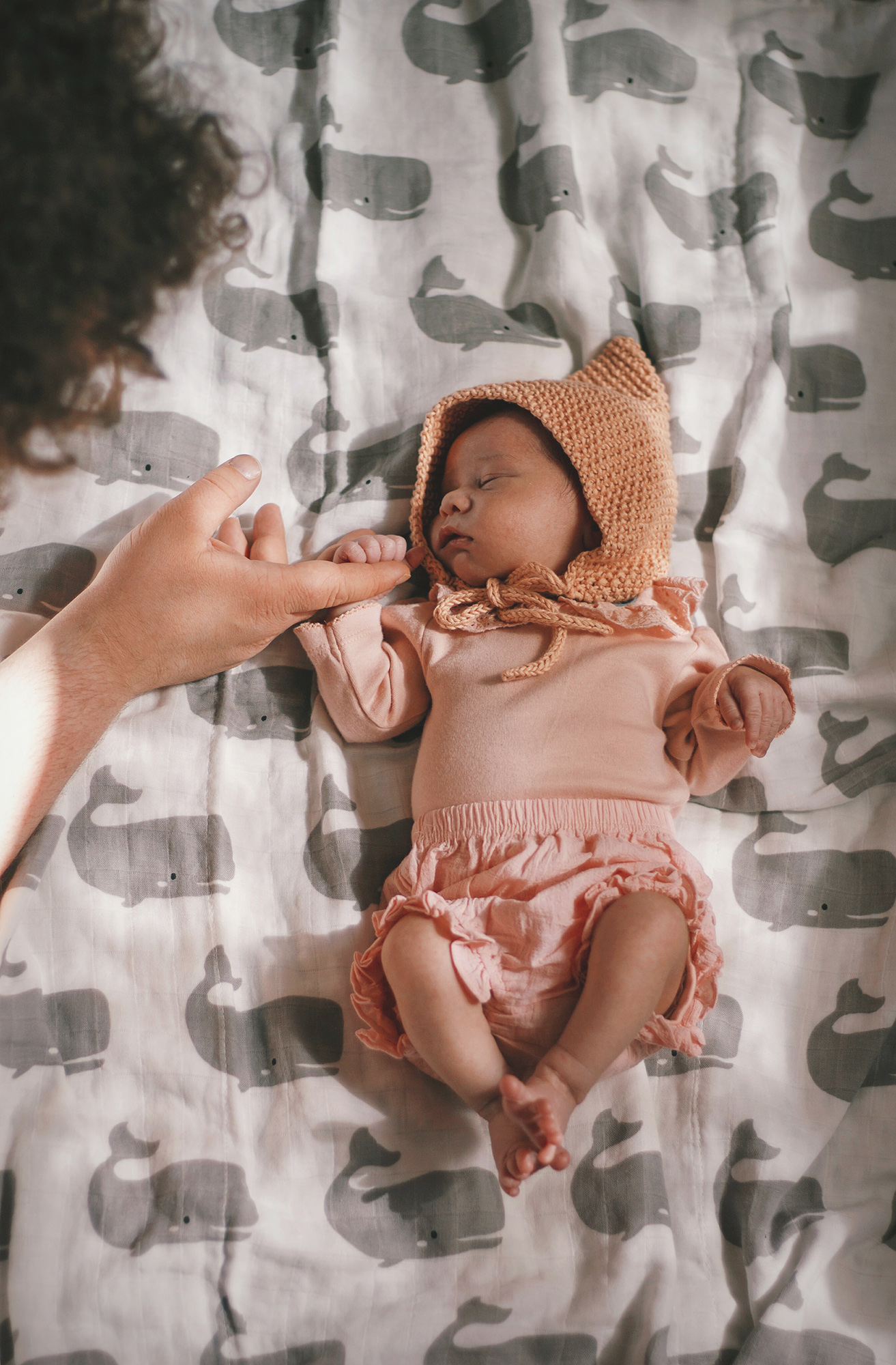 Lila at 10 days. A 10 day old baby wearing a pink bodysuit with a frilly collar, a pink pixie hat,  and pink frilly bloomers lying on a muslin blanket with a grey whale print.